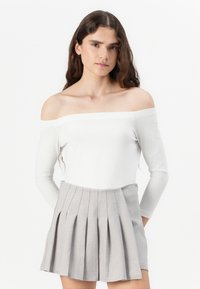 Top bianco alla Francis con maniche lunghe, abbinato a una gonna grigia plissettata. La gonna presenta pieghe strutturate e una vita liscia.