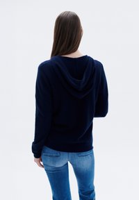 Felpa blu navy con una trama morbida, dotata di cappuccio con lacci e polsini a costine, abbinata a jeans azzurri.