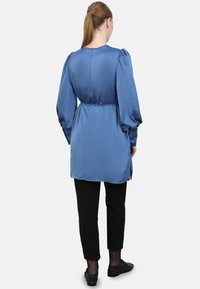 Blauw satijnen lange mouwen shirt met poffende mouwen, een taille met een strik, sluiting met knopen op de rug en zijsplitten, gecombineerd met zwarte slim-fit broek.