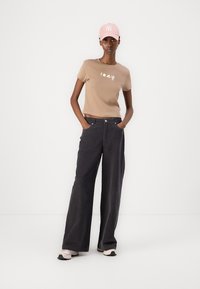 Beige cotton t-shirt with graphic print, paired with high-waisted black wide-leg jeans and light pink cap, worn with light-colored sneakers.