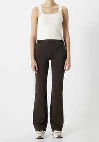 Kermanvärinen ribbitekstuuri tanktoppi neliskulmaisella pääntiellä, yhdistettynä korkea vyötäröiseen, levenevään ruskeaan housupariin. Asussa on siisti, minimalistinen muotoilu.