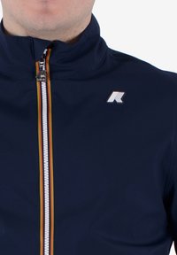 Giacca navy con zip realizzata in materiale leggero; presenta una zip bianca con accenti arancioni, gialli e verdi e un logo sul petto.