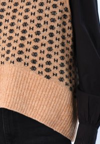 Strikket genser med en lys brun kropp med et teksturert svart mønster, ribbet kant og svarte, lange ermer med tilpassede mansjetter.