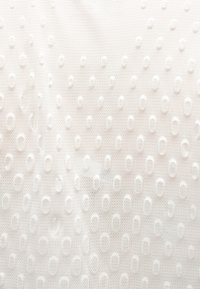 Tissu blanc texturé avec des motifs ovales en relief espacés uniformément et un fond en maille subtil.