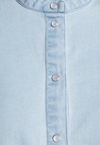 Light blue denim shirt featuring a button-down front with silver metallic snaps, smooth texture, and a rounded collar.