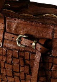 Primo piano di una borsa in pelle intrecciata marrone con una fibbia in ottone e dettagli con zip.