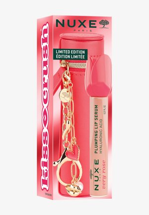Limitowana edycja serum do ust NUXE Paris z kwasem hialuronowym w różowym opakowaniu, w zestawie z czerwonym etui z złotym breloczkiem w kształcie serca.