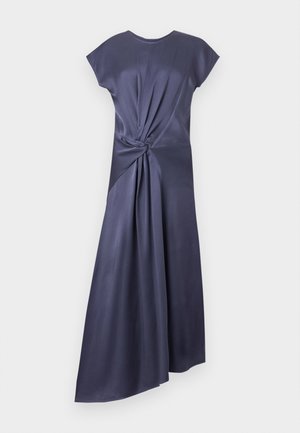 Moters su tatuiruotėmis mūvinti tamsiai mėlyną asimetrišką midi suknelę su šoniniu mazgo detalė ir juodus aukštakulnius sandalus su raišteliais.