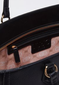 Interno di una borsa in pelle nera con un comparto con zip, fodera color rosa con un motivo a monogramma ripetuto e un'etichetta del marchio.
