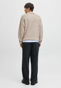 Beige strikket sweater med afslappet pasform, ribbede manchetter og rund krave. Parret med mørke, løstsiddende bukser.