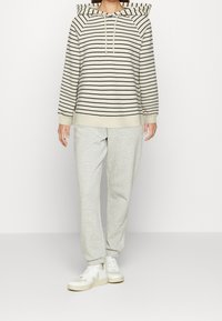 Pasiasty hoodie w kolorze kremowym i czarnym, z kapturem na sznurki i ściągaczami przy rękawach. Połączony z jasnoszarymi dresami i białymi sneakersami.