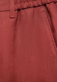 Red linen fabric with a textured finish, featuring a gathered waistband and stitching details, highlighting its soft and breathable quality.