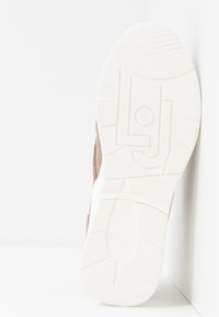 Brązowe zamszowe sneakersy z białą gumową podeszwą. Podeszwa ma teksturowany wzór i wypukłe logo marki. Czysty, nowoczesny design.