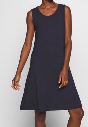 Sukienka bez rękawów w granatowym kolorze, sięgająca kolan, z okrągłym dekoltem, noszona przez osobę stojącą na jednolitym jasnym tle.