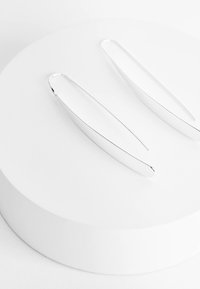 Boucles d'oreilles en métal argenté avec une forme allongée élégante et une surface lisse, présentant un design minimaliste sans ornements supplémentaires.