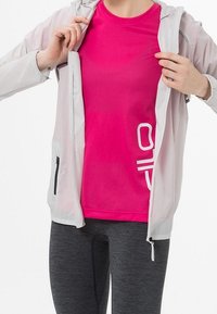 Chaqueta blanca ligera con cremallera sobre una camiseta deportiva de color rosa brillante. El conjunto incluye leggins de color gris oscuro. Acentos reflectantes en la chaqueta.