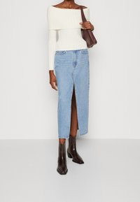 Maglione bianco a coste scoperto sulle spalle, gonna midi in denim azzurro chiaro con spacco frontale e stivaletti alla caviglia marroni scuri. Borsa marrone.