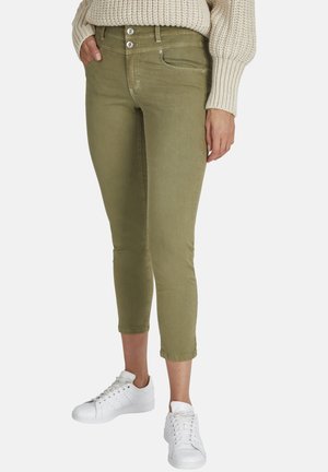 Pantalons courts vert olive avec une coupe slim, dotés d'un design à cinq poches classique, de deux boutons et de coutures contrastées ; portés avec des baskets blanches.