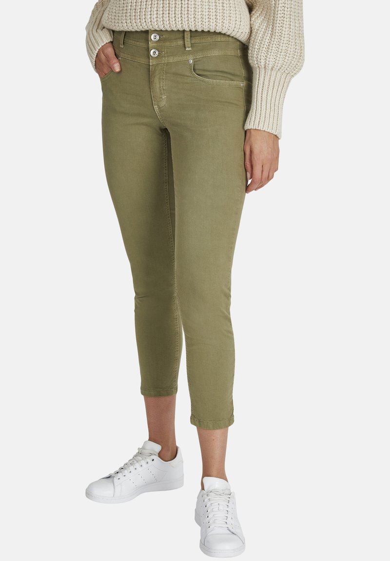 Pantalones cortos de color verde oliva con un corte ajustado, que presentan un diseño clásico de cinco bolsillos, dos botones y costuras en contraste; llevados con zapatillas blancas.