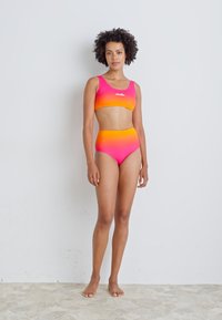 Dvojdielne plavky v prechodných odtieňoch ružovej a oranžovej. Obsahujú priliehavý crop top a plavky s vysokým pásom. Materiál vyzerá hladko a elasticky.