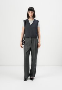Chaleco de punto azul marino sobre camiseta gris claro, combinado con pantalones de pierna ancha grises. Zapatos negros de punta y un pequeño bolso negro de hombro.