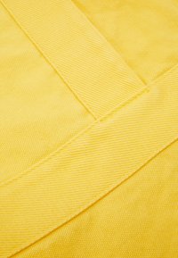 Żółta tkanina z nakładającymi się detalami pasków, ukazująca teksturowany splot i szwy.