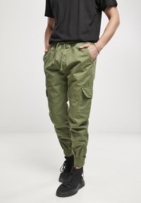 Pantalones cargo verdes con cinturilla elástica, cordón ajustable, puños ajustados y múltiples bolsillos laterales, combinados con zapatillas deportivas negras de caña alta.