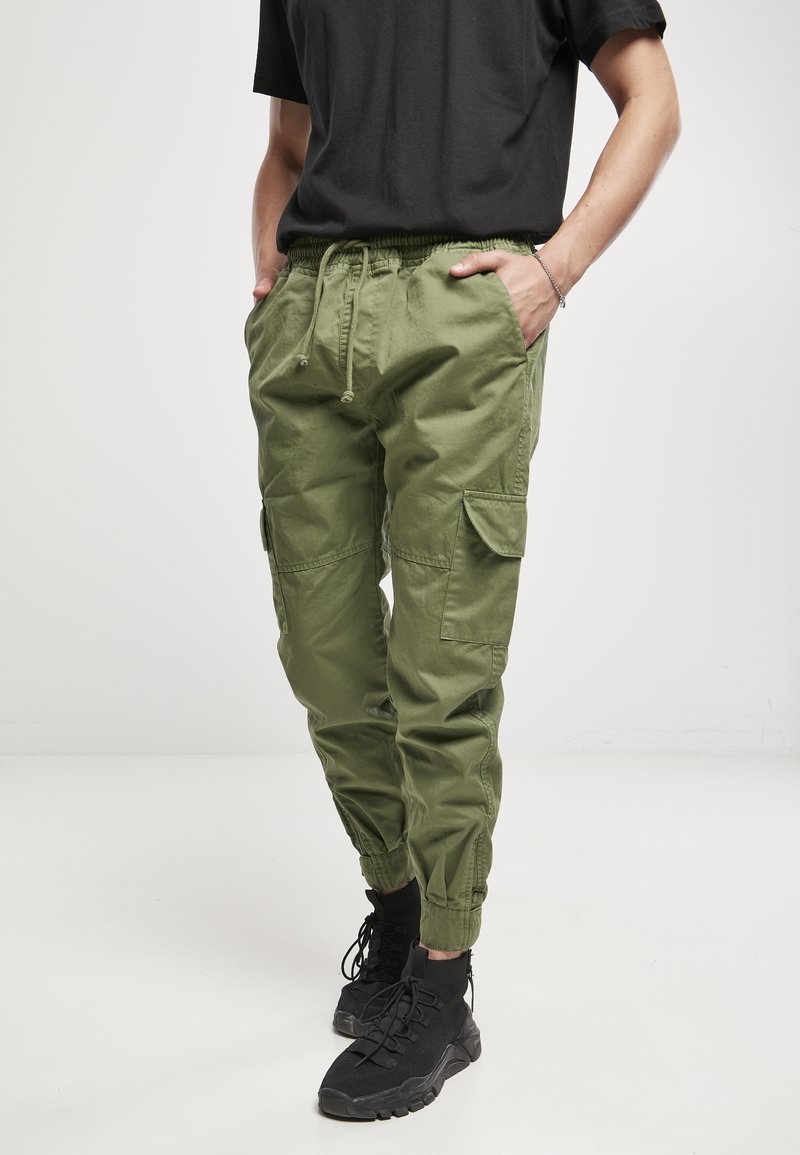Pantalones cargo verdes con cinturilla elástica, cordón ajustable, puños ajustados y múltiples bolsillos laterales, combinados con zapatillas deportivas negras de caña alta.