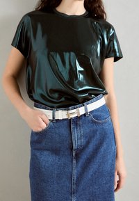 Glansig svart kortärmad skjorta med rund halsringning, kombinerad med en högmidjad blå denimkjol och ett vitt bälte.