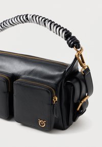 Μαύρη δερμάτινη τσάντα με σπειρωτή λαβή σε λευκό και μαύρο χρώμα. Διαθέτει δύο μπροστινές τσέπες με φερμουάρ και αξεσουάρ σε χρυσή απόχρωση. Συμπαγής σχεδίαση.