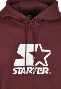Felpa color bordeaux con cappuccio e cordini, caratterizzata da un grande logo bianco stampato con la lettera "S" e una stella, realizzata in materiale di cotone.