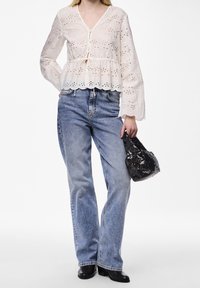 Blouse blanche brodée avec des manches évasées et une fermeture à boutons, associée à un jean en denim bleu clair et un sac à main noir à sequins.