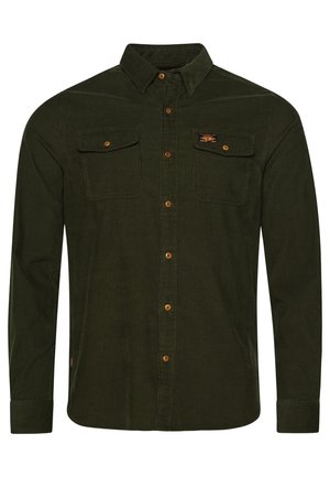 Camisa de pana verde oscuro de manga larga con cierre de botones, dos bolsillos en el pecho con solapas y un pequeño parche con logo en el bolsillo derecho.