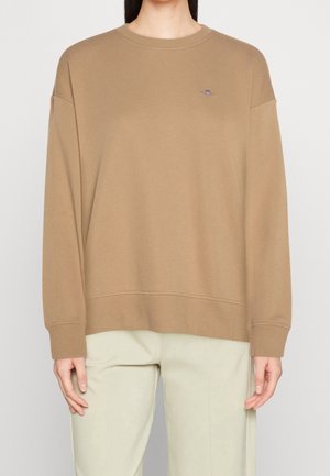 Sudadera marrón de gran tamaño con cuello y puños acanalados, que presenta un pequeño logotipo bordado en el lado izquierdo del pecho. Textura de tela suave.