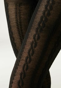 Le calze nere a fantasia presentano un design testurizzato con accenti a zigzag in rilievo, realizzate in materiale trasparente ed elastico per unindossabilità confortevole.