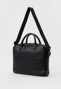 Sac noir structuré en matériau texturé, doté de deux poignées supérieures, d'une bandoulière réglable et d'une poche avant.