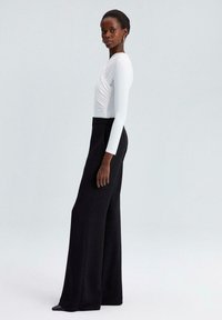 Body blanc à manches longues avec un design drapé associé à un pantalon noir à jambes larges. Texture lisse, style minimaliste et coupe ajustée.