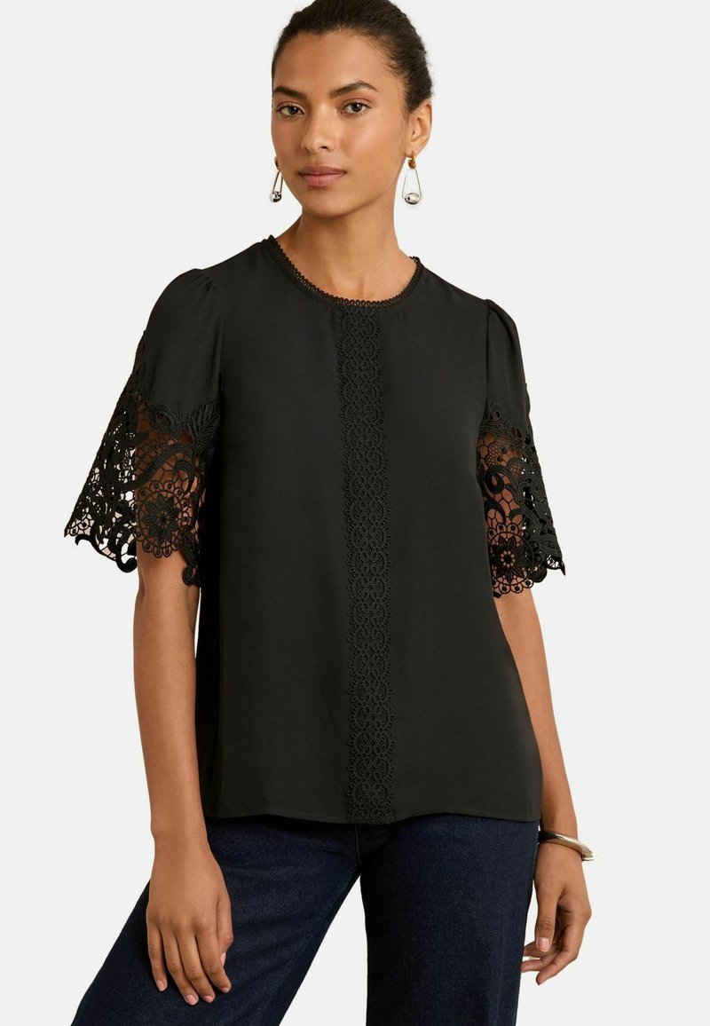 Blusa nera con maniche corte a sbuffo e raffinato pizzo, dalla consistenza morbida, con un dettaglio centrale in pizzo lungo la parte frontale.