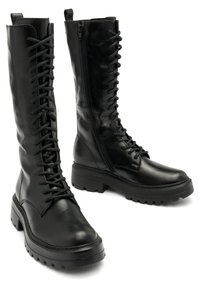Czarne skórzane botki do kolan z sznurowaniem i bocznym zamkiem błyskawicznym, na masywnej podeszwie z fakturowanym wykończeniem. Posiadają wzmocnione szwy i pętlę do zakładania.