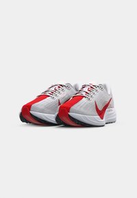 Les chaussures de course Nike présentent une tige en mesh gris respirant avec des accents rouges, une semelle blanche rembourrée et un profil en caoutchouc noir pour l'adhérence.