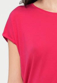 Κοντομάνικο, μπλουζάκι με στρογγυλή λαιμόκοψη σε έντονο ροζ χρώμα, κατασκευασμένο από απαλό, ελαφρύ ύφασμα. Διαθέτει γυρισμένα τελειώματα στα μανίκια και άνετη εφαρμογή.