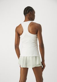 Hvit sportslig tank topp med racerback-design, sammen med et gjennomsiktig, lysegrønt skjørt, som viser glatt stoff og lagdelt tekstur.