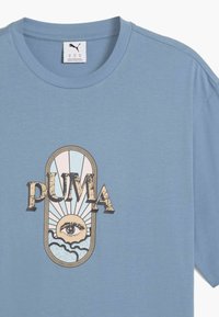 Lys blå bomulds T-shirt med et centralt grafisk design af et øje, sol, skyer og ordet "PUMA" i en struktureret, retro skrifttype.