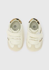 Scarpine per neonati in pelle crema e beige, con un accento a stampa leopardata sul retro, dotate di strap in Velcro e lacci. Etichetta della taglia visibile.