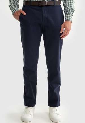 Marineblaue Chinos aus Baumwolle mit glatter Textur, ausgestattet mit Seitentaschen, geradem Schnitt und kombiniert mit weißen Sneakers.