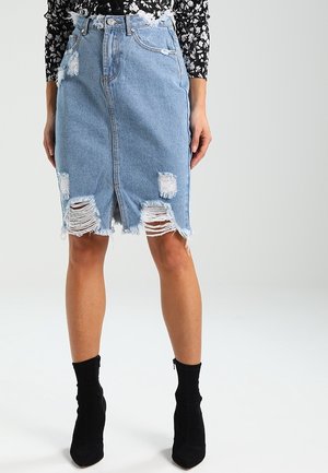 Vrouw draagt een lichtblauwe versleten spijkerrok tot op de knie met rafelige zoom en zwarte enkellaarzen met hak.