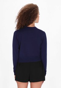 Tengerészkék, rövidített pulóver hosszú ujjal, bordázott aljjal és klasszikus kerek nyakkivágással, fekete sorttal párosítva. Egyszerű és testhezálló kialakítás.