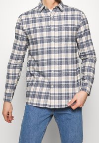 Kariertes Flanellhemd in Blau-, Beige- und Weißtönen. Verfügt über einen Button-Down-Kragen und eine Brusttasche, mit langen Ärmeln und lockerer Passform.