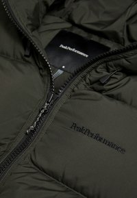 Olivengrøn dunjakke med lynlåslukning, der har en silkeagtig tekstur, broderet "PeakPerformance"-logo og høj krave.