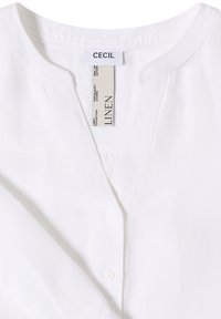 Chemise blanche en lin de CECIL avec col en V et devant boutonné, montrant les détails du col et de la texture du tissu.